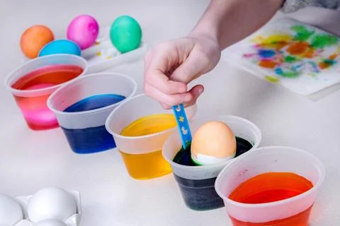 Kid hand paints eggs for easter holidays. Dyeing easter eggs at home. Child c Stock Photos