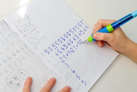 Kid hands doing math homework. Close up of young boy hand holding pen and wri Stock Photos