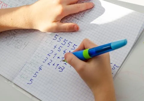 Kid hands doing math homework. Close up of young boy hand holding pen and wri Stock Photos