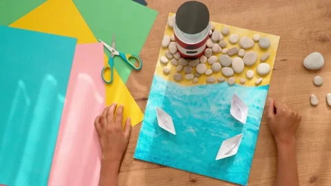 Kid hands make a lighthouse for school project at home. Top down view to wooden Stock Footage 133106804