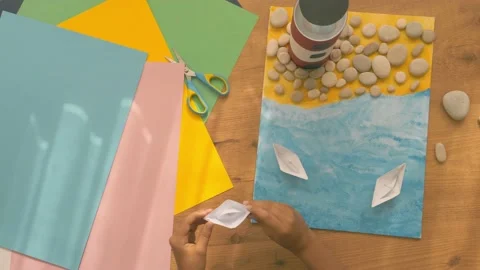 Kid hands make a lighthouse for school project at home. Top down view to wooden Stock Footage 133346523
