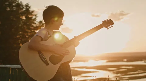 Kid having fun and play guitar at summer sunset, on high hill Stock Footage 65237536