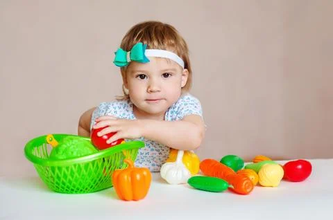 Kid having a table full of plastic food. Cheerful toddler eating healthy salad Stock Photos