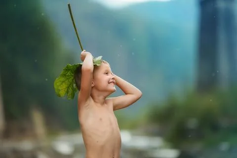 Kid hiding from the rain under a burdock Stock Photos