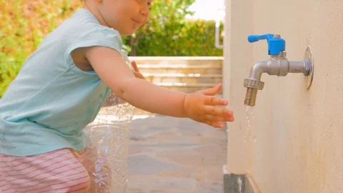 Kid holding empty plastic bottle near tap. Private kindergarten background Stock Footage 113509366