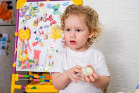 Kid holding hand painted Easter egg. Curly toddler girl enjoying spring holiday Stock Photos