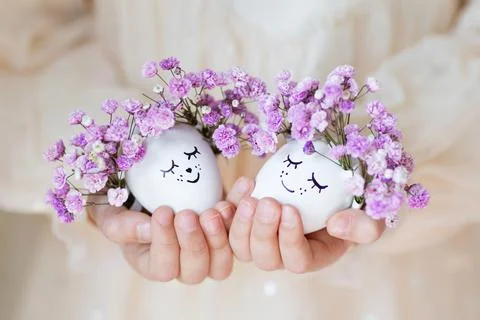Kid holding hands Cute Easter eggs with drawn faces and floral purple wreath Stock Photos