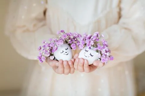 Kid holding hands Cute Easter eggs with drawn faces and floral purple wreath Stock-Fotos
