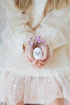 Kid holding hands Cute Easter eggs with drawn faces and floral purple wreath Foto stock