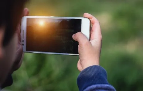 Kid holding a smartphone using both hands and taking a photo of sunset. Foto stock