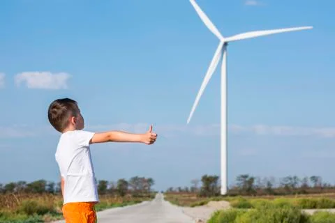 Kid is holding thumb up on background of wind turbine. Wind turbine generatin Stock Photos