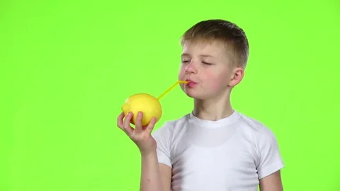 Kid holds a lemon through a straw drinking lemon juice, and shows a thumbs up Stock Footage 75792848