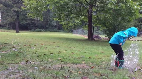 Kid jumping in lawn puddle during rain slow motion Stock Footage 94917059