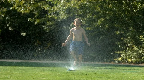 Kid jumping over sprinkler, slow motion Stock Footage