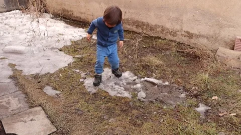 Kid jumping, stepping on mud and melting snow in backyard garden during spring Stock Footage 305994858