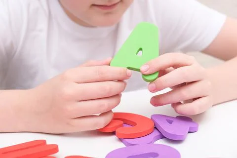 A kid learning letters and alphabet, he is sitting at a table and holding Stock Photos