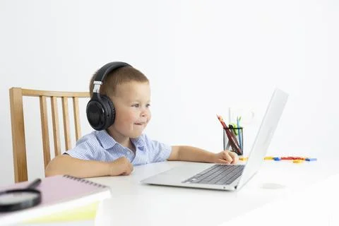 The kid learns and learns new things in the laptop while sitting at the table. Stock Photos