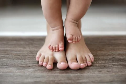 The kid learns to take first steps with the help of his mother Stock Photos