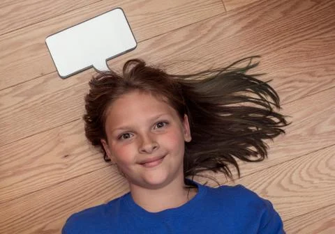 Kid lying on the floor with a blank thought bubble over her head. Stock Photos