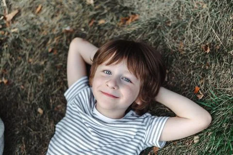 Kid lying on his back in the grass in park. Boy chilling on green lawn. Child Stock Photos