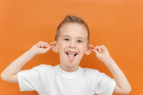 A kid makes a face on an orange background. Caucasian cheerful boy shows his Stock Photos