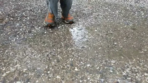 Kid in orange sneakers splashes in shallow puddle with slow motion effect Stock Footage 76799318