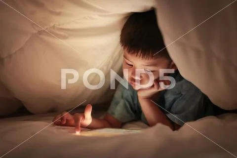 Kid play internet online game, under duvet. Stock Photos