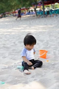 The kid is playing alone on a white beach with a bucket and a sand shovel. cl Foto stock