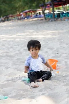 The kid is playing alone on a white beach with a bucket and a sand shovel. cl Foto stock