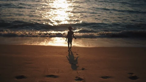 Kid playing and dancing on sandy beach with sun behind Stock Footage 119116441