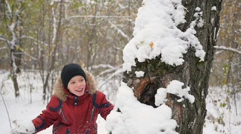 Kid playing throwing snowballs from behind tree in winter Park Vidéo 68848497