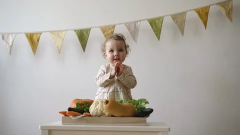 Kid playing with vegetables, clapping and smiling while sitting at the table Stock Footage 128071799