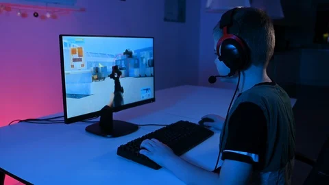 Kid plays esport game while sitting in front of pc with headset and keyboard Stock Footage 100725959