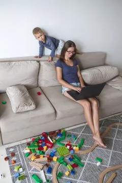 Kid plays on the sofa while mom works with laptop, distracts and Stock Photos