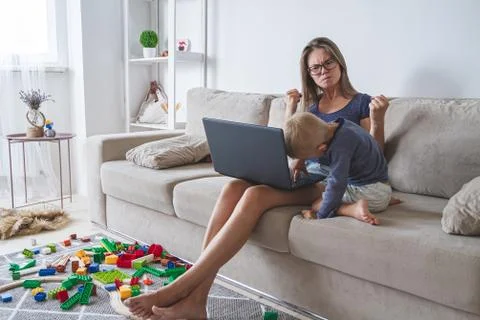 Kid plays on the sofa while mom works with laptop, distracts and Foto stock