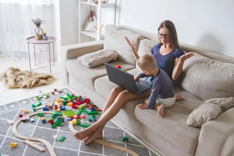 Kid plays on the sofa while mom works with laptop, distracts and Stock Photos