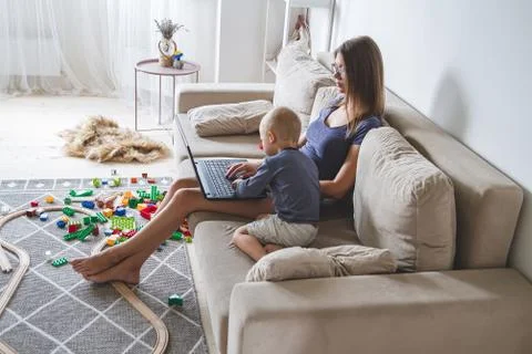 Kid plays on the sofa while mom works with laptop, distracts and Stock Photos