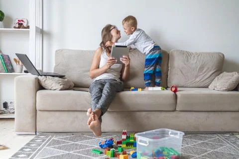 Kid plays on the sofa while mom works with tablet, distracts and Stock Photos