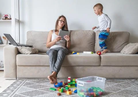 Kid plays on the sofa while mom works with tablet, distracts and Stock Photos