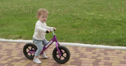 Kid rides quickly while sitting on a children's scooter Stock Footage 252310104