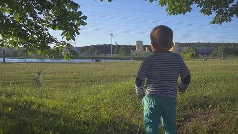 Kid runs from the camera on the green grass. Little boy takes his first steps on Stock Footage 90423872
