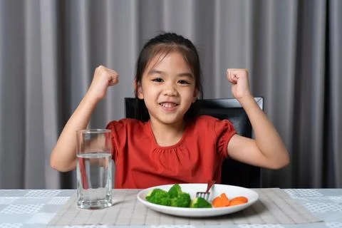 Kid shows strength of eats vegetables and nutritious food. Stock Photos