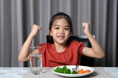 Kid shows strength of eats vegetables and nutritious food. Stock Photos