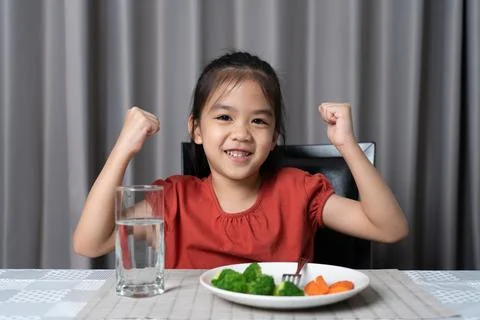 Kid shows strength of eats vegetables and nutritious food. Stock Photos