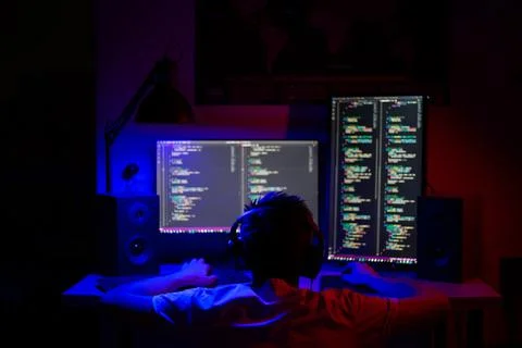 A kid sits at a computer in a room at a table at night with blue lighting and Stock Photos