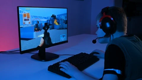 Kid sits in front of pc with headset and keyboard playing an esport video game Stock Footage 100726226