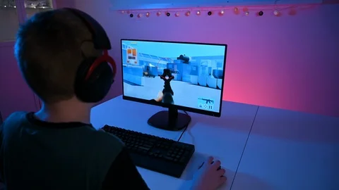 Kid sits in front of pc with headset and keyboard playing an esport video game Stock Footage 100726304