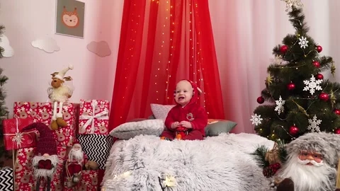 The kid is sitting on the bed in a red suit. New Year. Holiday. Christmas. Stock Footage 165779675