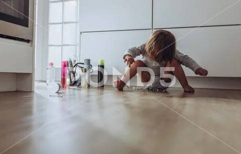 Kid sitting on floor at home playing with cosmetic bottles Stock Photos