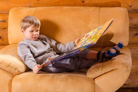 Kid sitting on sofa with a book Stock Photos